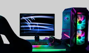 Gracz wpatrzony w monitor z niebieskimi smugami światła. Obok komputer z kolorowymi wentylatorami. Idealne miejsce na fajne słowa po angielsku na nick.