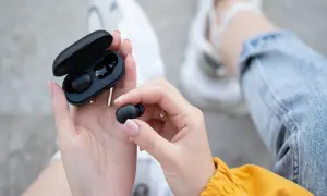 Dłonie trzymają czarne słuchawki bluetooth i etui. Dowiedz się, jak zresetować słuchawki bluetooth, gdy masz problem z połączeniem.