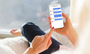 Kobieta trzyma telefon, na którym widać rozmowę na Messengerze. Pokazuje, jak aktywować tę funkcję, pisząc wiadomość.