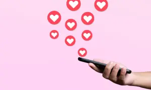 Darmowe lajki na Instagramie? Smartfon w dłoni, a z niego wypływają serduszka, symbolizujące popularność i uznanie.