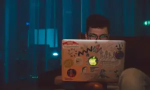 Chłopak z okularami szuka angielskich nicków do gier na laptopie ozdobionym naklejkami.