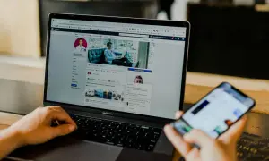 Osoba przegląda profil na Facebooku na laptopie, zastanawiając się, czy usunięcie znajomego z FB jest widoczne. Na telefonie widać powiadomienia.