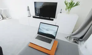 Nowoczesny salon z MacBookiem na pufie i telewizorem w tle. Dowiedz się, jak połączyć MacBooka z telewizorem, by cieszyć się filmami na dużym ekranie.