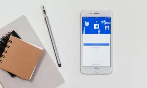 Smartfon z ekranem logowania Messengera. Jak odzyskać hasło do Messengera bez Facebooka? Notatnik i długopis obok.