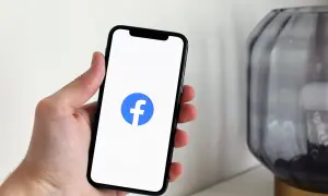 Dłoń trzyma smartfon z logo Facebooka. Dowiedz się, jak dodać ogłoszenie na FB, by sprzedać lub kupić rzeczy.