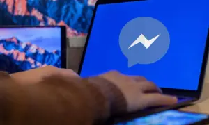 Dłoń na laptopie z logo Messengera. Dowiedz się, jak odzyskać cofniętą wiadomość Messenger.