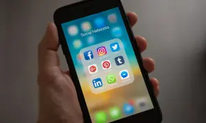 Dłoń trzyma smartfon z ikonami aplikacji społecznościowych. Widoczna ikona Facebooka, która pomoże Ci dowiedzieć się, jak dołączyć do grupy na FB.