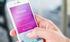 Dłoń trzyma smartfon z ekranem logowania Instagram. Dowiedz się, jak dodać zdj na Insta, logując się lub tworząc konto.