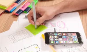 Ręka pisze na zielonej karteczce, obok leży smartfon i szkice. To inspiracja, jak wymyślić ksywkę.