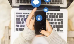 Dłonie trzymające smartfon nad klawiaturą laptopa. Ikony komunikatorów unoszą się w powietrzu. Zastanawiasz się, dlaczego na Messengerze nie widać, kiedy ktoś był aktywny?