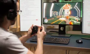 Gracz z kontrolerem w ręku, grający w grę na monitorze. Na drugim ekranie czat z komentarzami, gdzie można znaleźć fajne polskie nicki do gier.