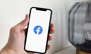 Dłoń trzyma smartfon z logo Facebooka. Chcesz wiedzieć, jak zablokować widoczność na FB?
