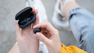 Dłonie trzymają czarne słuchawki bluetooth i etui. Dowiedz się, jak zresetować słuchawki bluetooth, gdy masz problem z połączeniem.