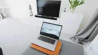 Nowoczesny salon z MacBookiem na pufie i telewizorem w tle. Dowiedz się, jak połączyć MacBooka z telewizorem, by cieszyć się filmami na dużym ekranie.
