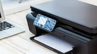 Czarny drukarka z ekranem dotykowym i laptopem obok. Dowiedz się, jak zmienić wi-fi w drukarce, aby drukować bezprzewodowo.