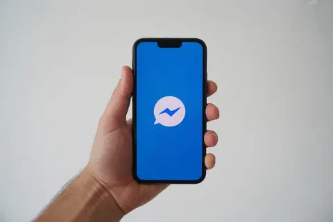 Dłoń trzyma smartfon z niebieskim ekranem i ikoną Messengera. Zastanawiasz się, dlaczego nie widzę aktywności osoby na Messengerze?