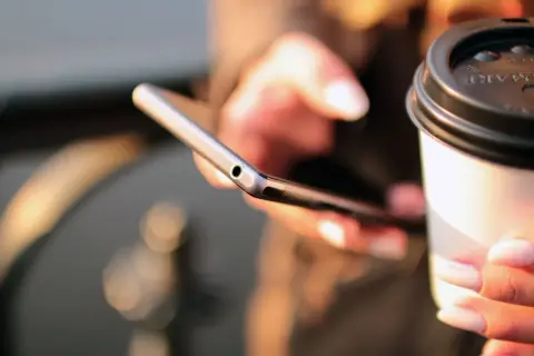 Kobieta trzyma telefon i kubek kawy, szukając informacji, jak się doładowuje Play.