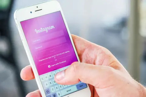 Dłoń trzyma smartfon z ekranem logowania Instagram. Widoczna opcja "Zapomniane dane logowania?" podpowiada, jak odzyskać hasło na Instagramie.