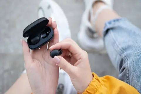 Dłonie trzymają czarne słuchawki bluetooth i etui. Dowiedz się, jak zresetować słuchawki bluetooth, gdy masz problem z połączeniem.