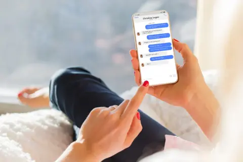 Kobieta trzyma telefon, na którym widać rozmowę na Messengerze. Pokazuje, jak aktywować tę funkcję, pisząc wiadomość.