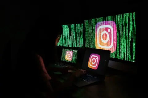 Osoba pracuje przy komputerze, na ekranach widnieje logo Instagrama i zielony kod. Szuka informacji, jak odzyskać zhakowane konto na Instagramie.