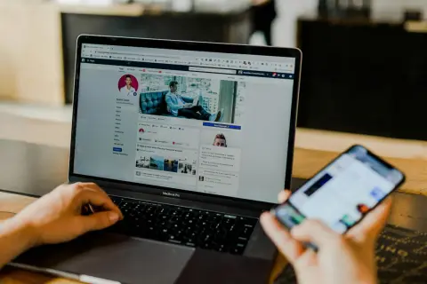 Osoba przegląda profil na Facebooku na laptopie, szukając informacji, jak usunąć znajomego na FB. Obok leży smartfon.