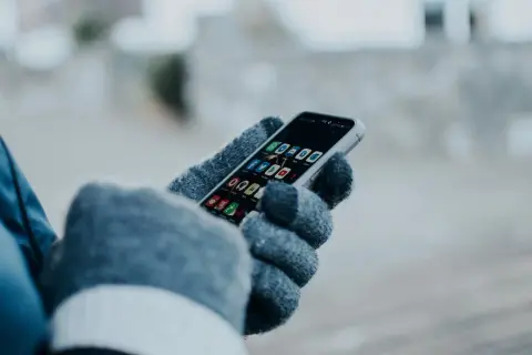 Ręka w rękawiczce trzyma smartfon z ikonami aplikacji. Chcesz wiedzieć, jak sprawdzić czy ktoś jest aktywny na Facebooku?