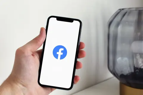 Dłoń trzyma smartfon z logo Facebooka. Chcesz wiedzieć, jak wyłączyć widoczność na FB?
