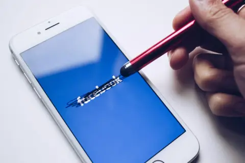 Ręka rysuje stylusem na ekranie telefonu logo Facebooka. Zastanawiasz się, jak odzyskać konto Messenger?