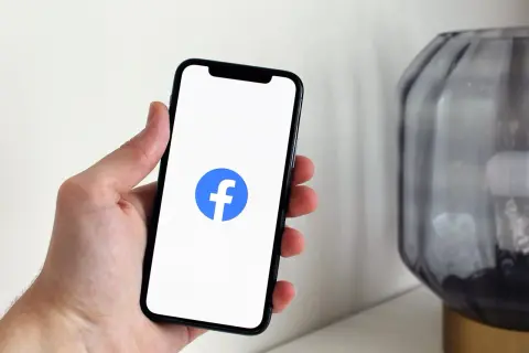 Dłoń trzyma smartfon z logo Facebooka. Dowiedz się, jak sprawdzić relacje na Facebooku, aby być na bieżąco.