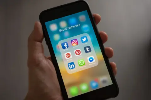 Dłoń trzyma smartfon z ikonami sieci społecznościowych. Szukasz nicków dla chłopaka na Messengera? Tutaj znajdziesz inspiracje!