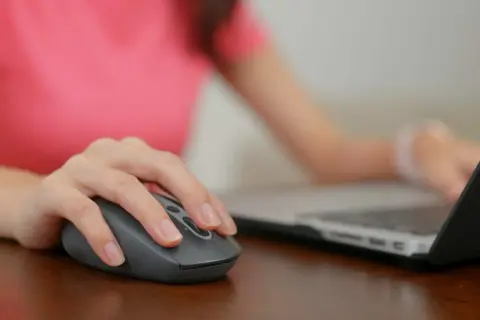 Dłoń na myszce, która jest podłączona do laptopa. Wiesz już, gdzie podłączyć myszkę do komputera.