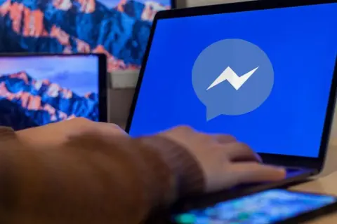Dłoń na laptopie z logo Messengera. Dowiedz się, jak odzyskać cofniętą wiadomość Messenger.