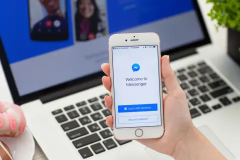Dłoń trzyma iPhone'a z ekranem powitalnym Messengera. Dowiedz się, jak ustawić dymki czatu Messenger na iPhone.