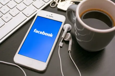 Telefon z Facebookiem, klawiatura i kawa. Dowiedz się, jak założyć konto szkoły na Facebooku, by być bliżej uczniów.
