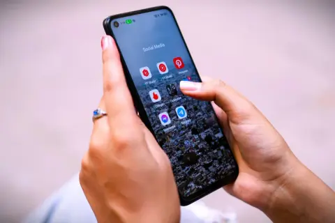 Dłonie trzymają telefon z ikonami aplikacji społecznościowych. Zastanawiasz się, jak trwale usunąć wiadomości z Messengera?