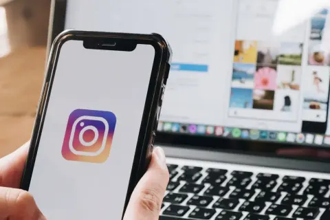 Telefon z logo Instagram. Na ekranie laptopa widać siatkę zdjęć, jakbyś chciał dowiedzieć się, jak wstawić czyjąś relację na swoją.