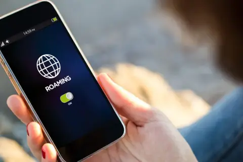 Telefon pokazuje ikonę globu i napis "ROAMING" z włączonym przełącznikiem. To oznacza, że funkcja roamingu jest aktywna.