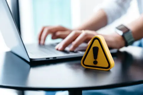 Żółty trójkąt z wykrzyknikiem obok laptopa, sugerujący problem, dlaczego nie mogę wylogować się z Facebooka.