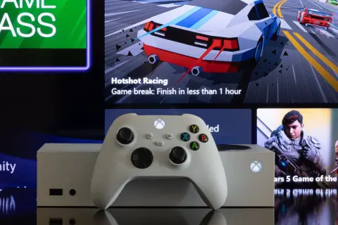 Biały kontroler Xbox i konsola na tle ekranu z menu Game Pass i grami. Dowiedz się, jak pobierać gry na Xbox, korzystając ze sklepu i Game Pass.
