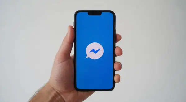 Dłoń trzyma smartfon z niebieskim ekranem i ikoną Messengera. Zastanawiasz się, dlaczego nie widzę aktywności osoby na Messengerze?