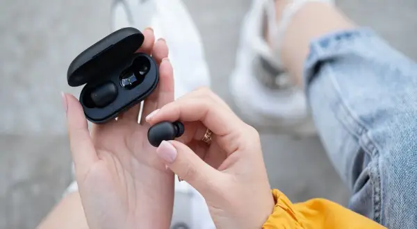 Dłonie trzymają czarne słuchawki bluetooth i etui. Dowiedz się, jak zresetować słuchawki bluetooth, gdy masz problem z połączeniem.