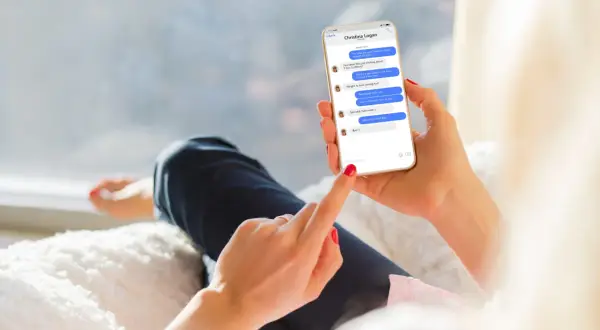 Kobieta trzyma telefon, na którym widać rozmowę na Messengerze. Pokazuje, jak aktywować tę funkcję, pisząc wiadomość.
