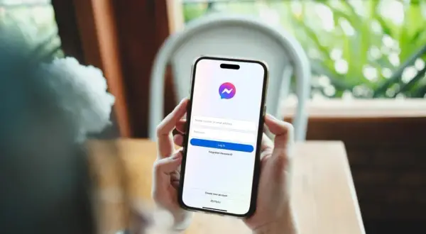 Dłonie trzymają smartfon z ekranem logowania Messengera. Dowiedz się, jak założyć czat na Messengerze, tworząc nowe konto.