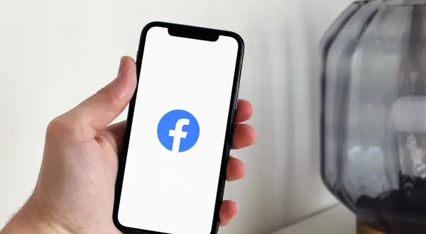 Dłoń trzyma smartfon z logo Facebooka. Chcesz wiedzieć, jak wyłączyć widoczność na FB?