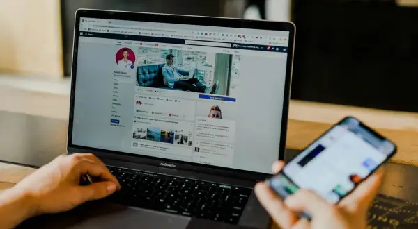 Osoba przegląda profil na Facebooku na laptopie, zastanawiając się, czy usunięcie znajomego z FB jest widoczne. Na telefonie widać powiadomienia.