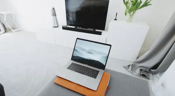 Nowoczesny salon z MacBookiem na pufie i telewizorem w tle. Dowiedz się, jak połączyć MacBooka z telewizorem, by cieszyć się filmami na dużym ekranie.