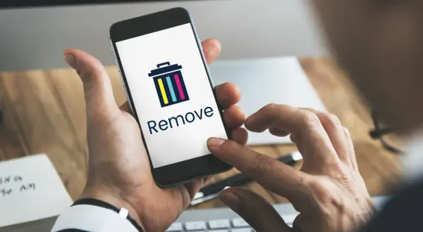 Dłoń trzyma smartfon z ikoną kosza i napisem "Remove". Dowiedz się, jak usunąć członka z grupy na Messengerze.