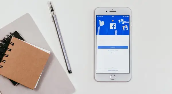 Smartfon z ekranem logowania Messengera. Jak odzyskać hasło do Messengera bez Facebooka? Notatnik i długopis obok.