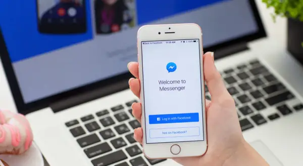 Jak włączyć dymki czatu w Messengerze na iPhone? Na ekranie telefonu widać ekran logowania do Messengera.